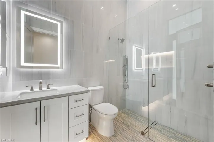 Bathroom featuring tile walls, toilet, a stall shower, and vanity