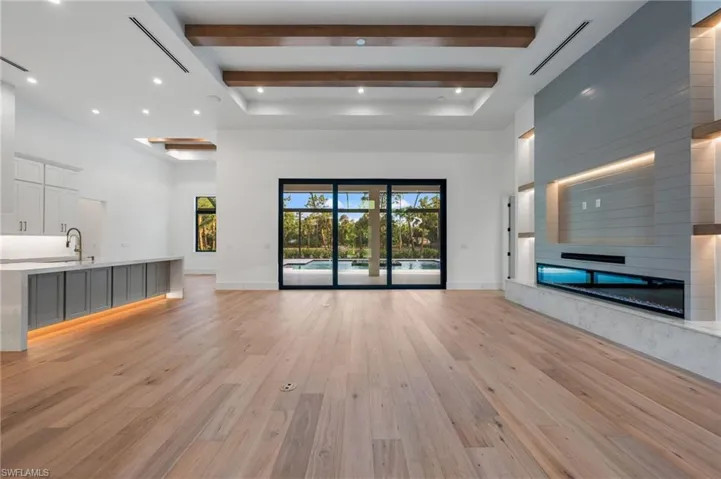 Unfurnished living room with a towering ceiling, light wood-style flooring, a sink, and beam ceiling