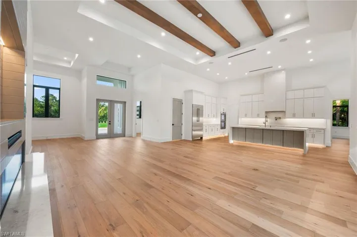 Unfurnished living room featuring beamed ceiling, light wood finished floors, a towering ceiling, and a sink