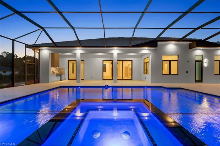 View of swimming pool featuring elevator, a patio area, a pool with connected hot tub, and glass enclosure