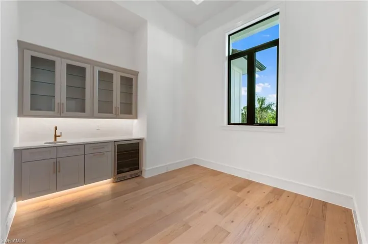 Bar with baseboards, wet bar, light wood finished floors, beverage cooler, and a sink