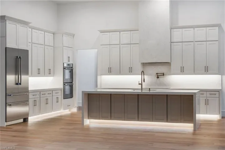 Kitchen featuring appliances with stainless steel finishes, an island with sink, light wood-style flooring, decorative backsplash, and a sink