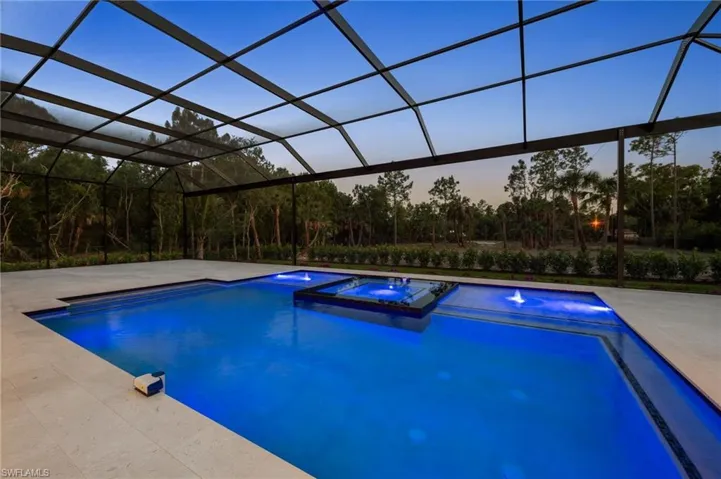 Pool at dusk featuring a lanai, a patio, and a pool with connected hot tub