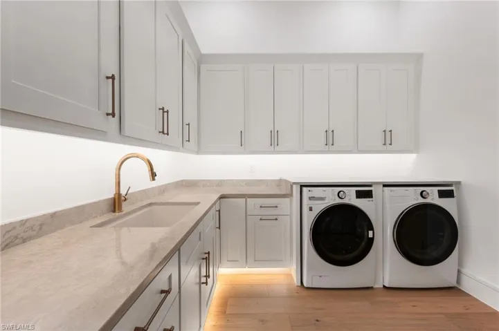 Clothes washing area featuring a sink, light wood-type flooring, washer and dryer, and cabinet space