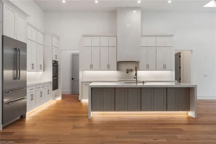Kitchen featuring light wood-type flooring, a towering ceiling, white cabinetry, appliances with stainless steel finishes, and a sink