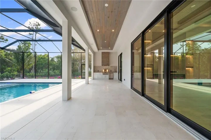 Pool featuring glass enclosure, a patio, and area for grilling