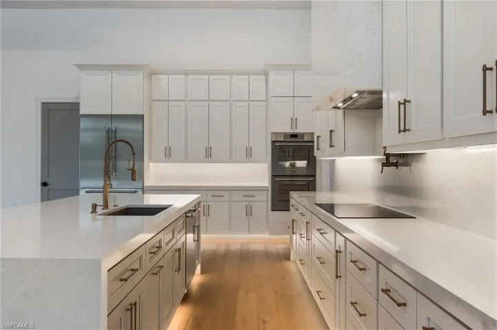 Kitchen featuring white cabinets, stainless steel built in fridge, double wall oven, light wood finished floors, and backsplash