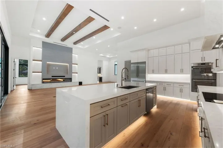 Kitchen with light wood-style flooring, appliances with stainless steel finishes, a high ceiling, a sink, and beam ceiling