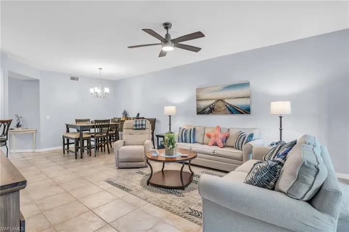 Tiled living room with ceiling fan with notable chandelier