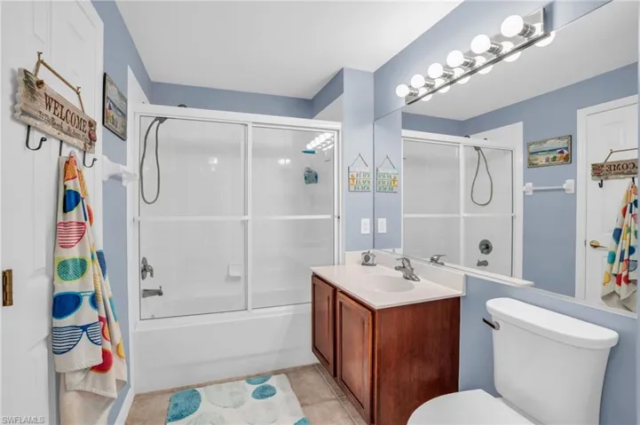 Full bathroom featuring enclosed tub / shower combo, tile floors, vanity, and toilet