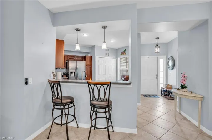 Kitchen with kitchen peninsula, a kitchen breakfast bar, hanging light fixtures, stainless steel fridge, and light tile floors