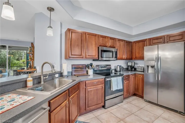 Kitchen featuring a tray ceiling, pendant lighting, light tile floors, sink, and appliances with newer stainless steel finishes