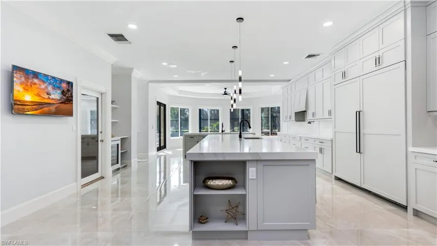 Kitchen with open shelves, a large island, paneled fridge, ornamental molding, and light stone countertops