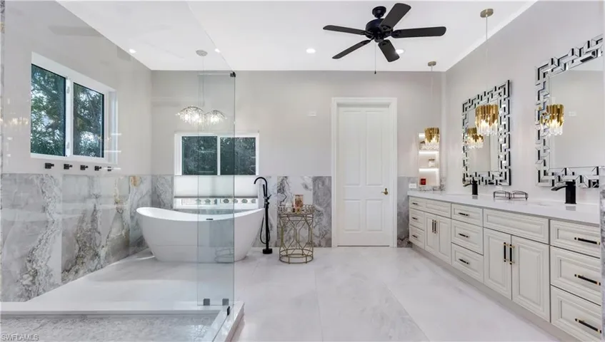 master bathroom featuring tile walls, double vanity, a wainscoted wall, a freestanding tub