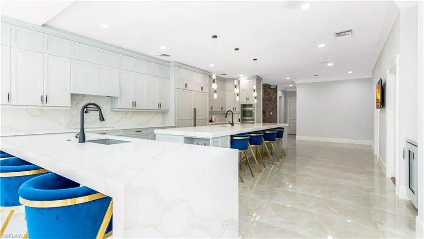 Kitchen featuring a kitchen bar, light stone counters, backsplash, ornamental molding, and pendant lighting
