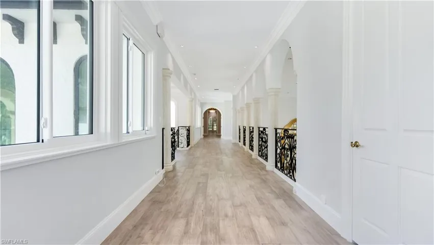 Hallway with arched walkways, light wood-style flooring, ornamental molding, and an upstairs landing