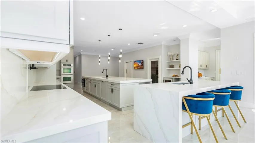 Kitchen featuring light stone counters, a kitchen bar, crown molding, stainless steel double oven, and decorative light fixtures