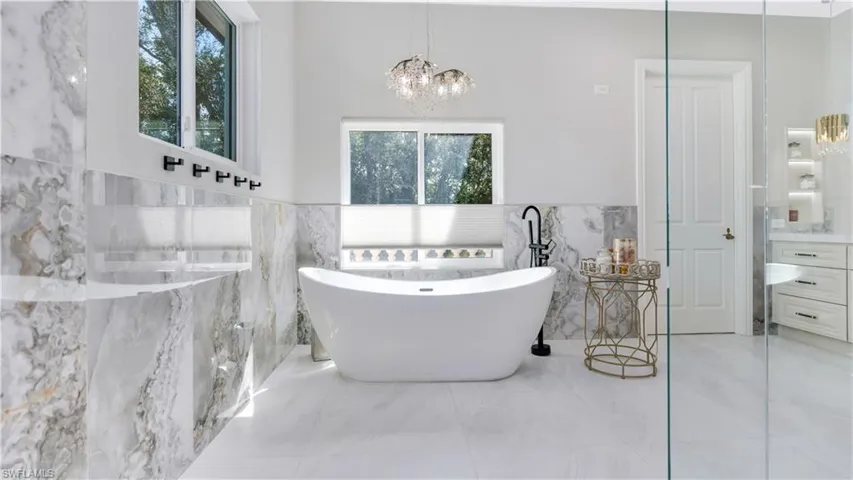 Bathroom with a wainscoted wall, tile walls, a freestanding tub, vanity, and a chandelier