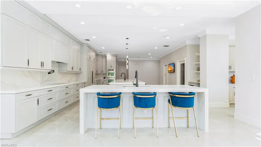 Kitchen featuring light stone counters, a breakfast bar area, crown molding, decorative backsplash, and hanging light fixtures