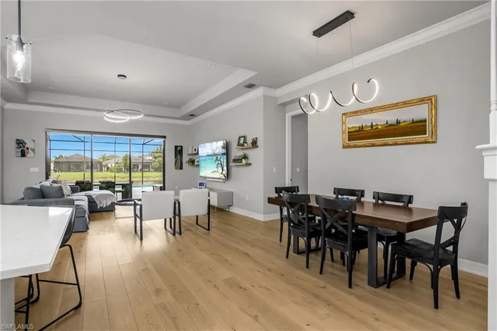 Dining space with a raised ceiling, light wood-style floors, and ornamental molding