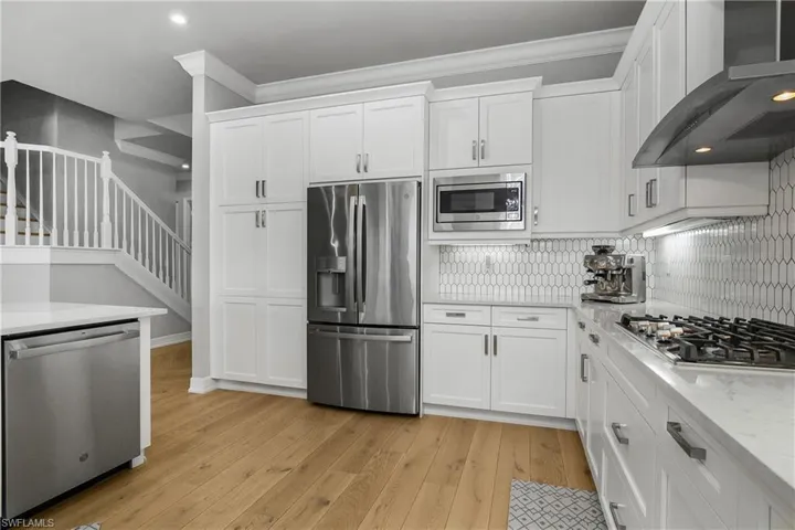 Kitchen with appliances with stainless steel finishes, wall chimney range hood, light stone countertops, white cabinets, and recessed lighting