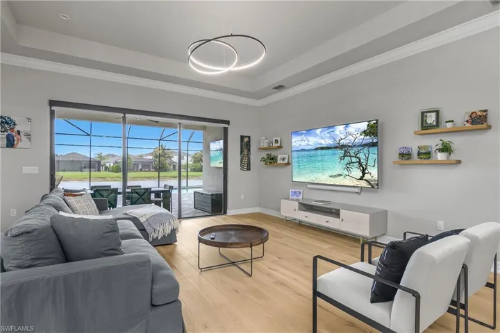 Living room featuring a raised ceiling, light wood-style floors, crown molding, and a sunroom