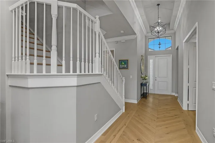 Entrance foyer with ornamental molding, wood finished floors, stairs, a towering ceiling, and a chandelier