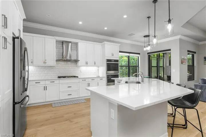 Kitchen featuring ornamental molding, light wood-style floors, backsplash, wall chimney range hood, and white cabinetry