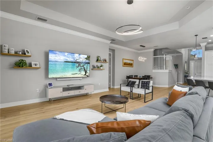 Living area with a raised ceiling, light wood-type flooring, and crown molding