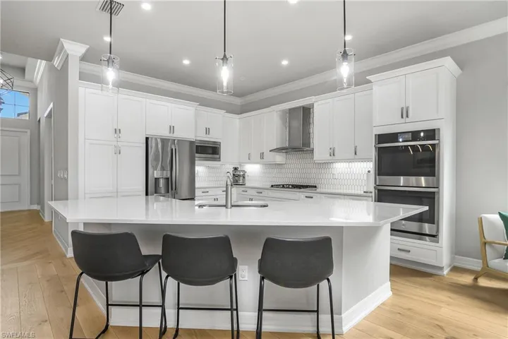 Kitchen with white cabinetry, stainless steel appliances, wall chimney exhaust hood, decorative backsplash, and light wood-style flooring