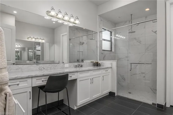 Bathroom featuring a marble finish shower, vanity, dark tile patterned flooring, and recessed lighting