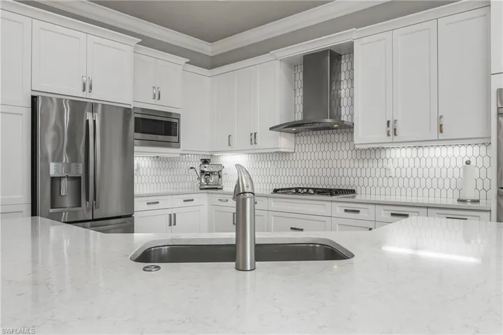 Kitchen with appliances with stainless steel finishes, decorative backsplash, crown molding, wall chimney exhaust hood, and white cabinetry