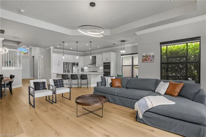 Living room with a raised ceiling, crown molding, light wood finished floors, and recessed lighting