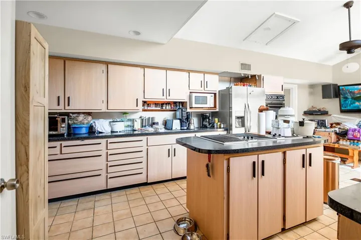 Kitchen with light brown cabinets, a center island, light tile flooring, and stainless steel fridge with ice dispenser