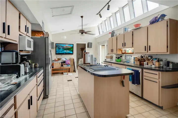 Kitchen with ceiling fan, stainless steel appliances, track lighting, light tile floors, and a center island