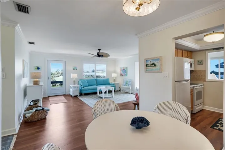 Open-concept living area featuring wood-finish flooring, a ceiling fan, and crown molding
