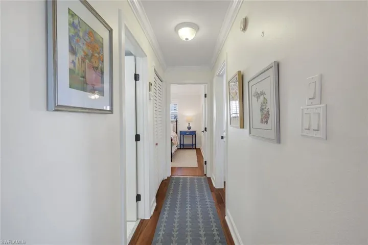 Hallway featuring wood-finish flooring, white trim, and crown molding