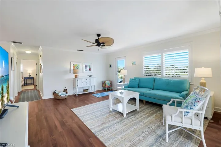 Spacious living area featuring wood-finish flooring, white plantation shutters, crown molding, and a ceiling fan with natural woven blades