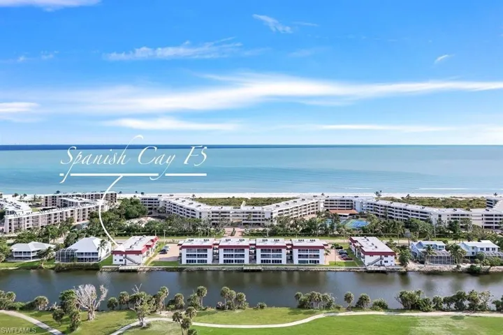 Waterfront condominium community with direct beach access, featuring multiple residential buildings, lush landscaping, and recreational amenities including a tennis court