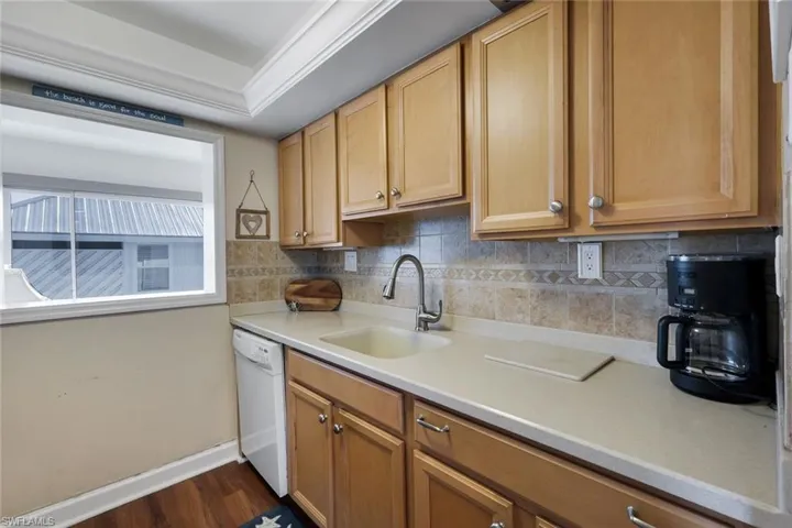 Kitchen area featuring wood-finish cabinetry with silver-tone hardware, a light-toned countertop, and a tiled backsplash