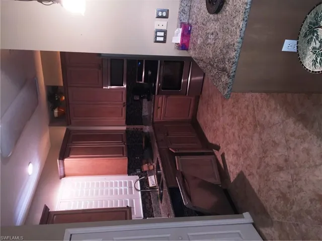 The kitchen features granite countertops, dark wood cabinetry, stainless steel appliances, and a tiled floor