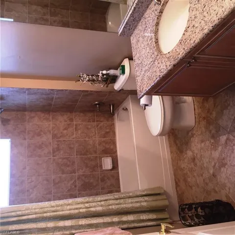 Bathroom featuring a vanity with a granite countertop and an undermount sink, a toilet, a tiled shower, and a window with a valance