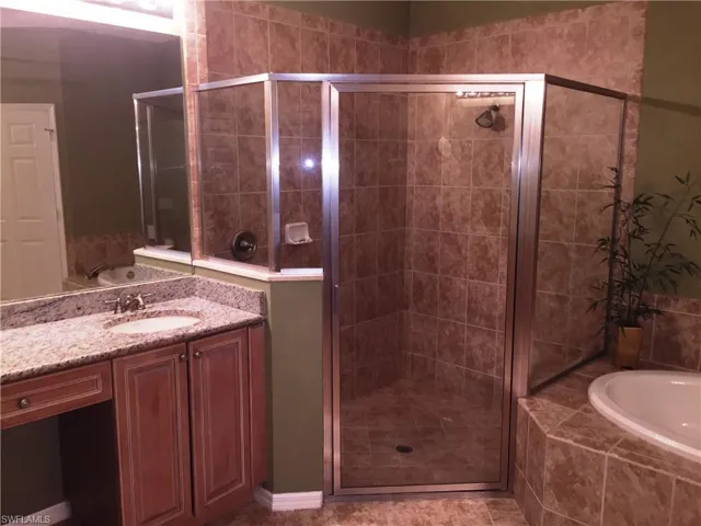 Bathroom featuring a corner shower with glass enclosure, a vanity with a light-colored countertop and undermount sink, and a built-in bathtub