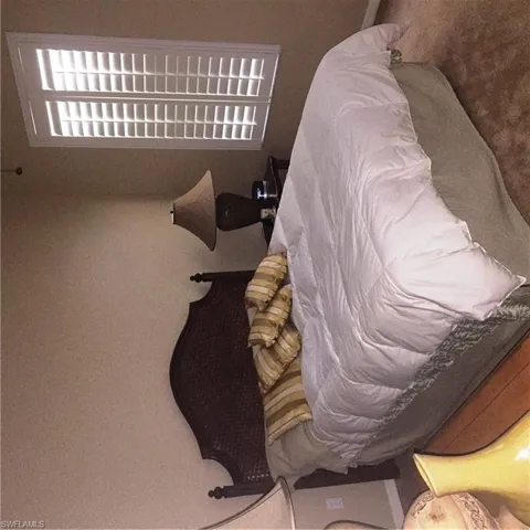 This room features a window with white plantation shutters, a dark wood headboard, and a bedside lamp with a fabric shade