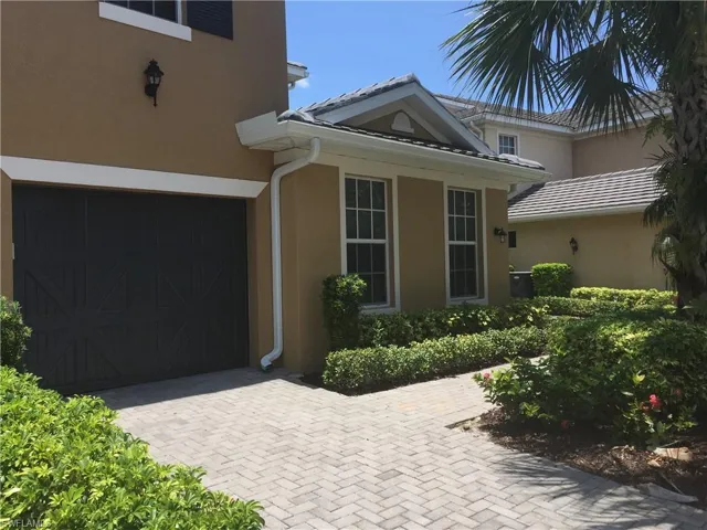 The property features a paver driveway, a dark garage door, and well-maintained shrubs
