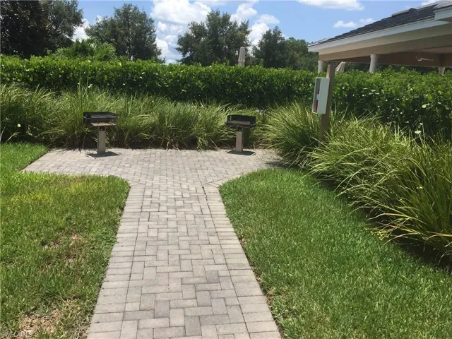 Outdoor grilling area featuring two grills, a paver walkway, and lush landscaping