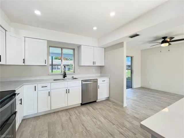 Kitchen with white cabinets, sink, stainless steel dishwasher, and light wood-type flooring