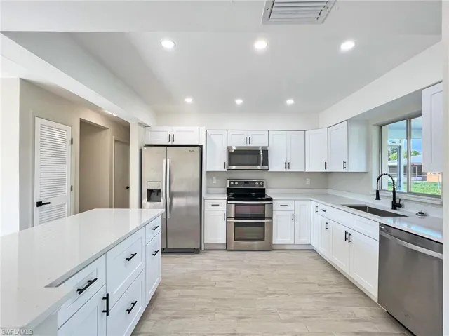 Kitchen with light hardwood / wood-style floors, appliances with stainless steel finishes, white cabinets, light stone counters, and sink