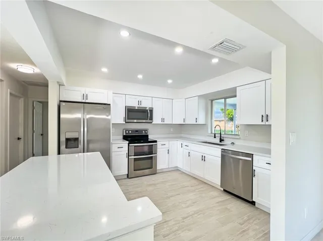 Kitchen featuring light stone counters, light hardwood / wood-style flooring, stainless steel appliances, white cabinetry, and sink