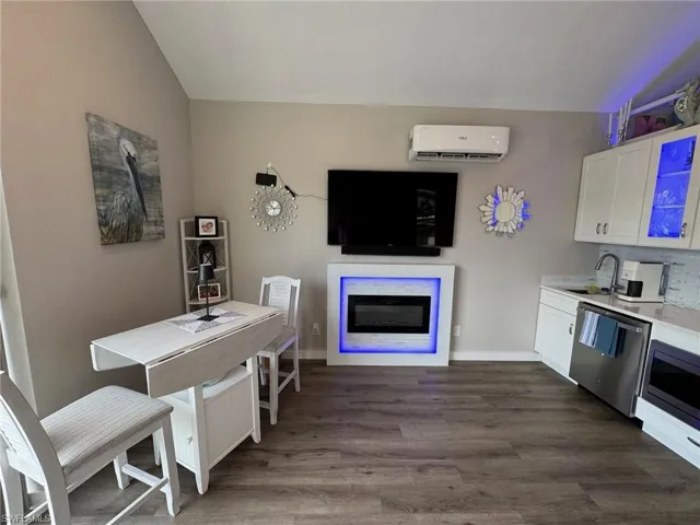 Kitchen with a wall unit AC, stainless steel appliances, white cabinetry, sink, and dark hardwood / wood-style floors